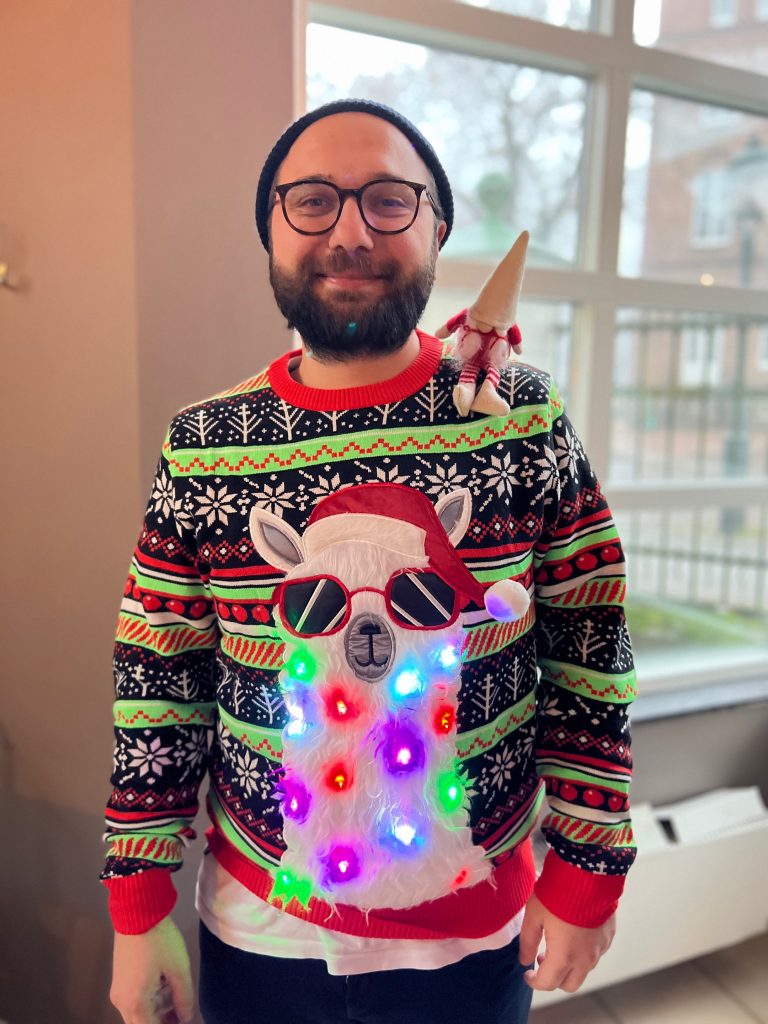 Sinan posing with his winning sweater in the "ugliest Christmas sweater competition".